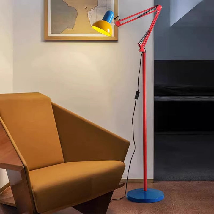 Stehlampe mit Gelenkarm in Rot, blauer Basis und gelbem Schirm neben Sessel