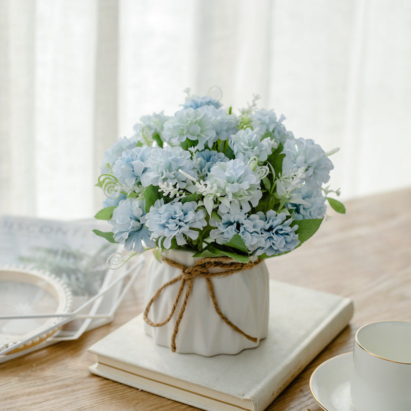 Seidenblumenarrangement in einem mit Schnur umwickelten Keramikpflanzer als Tischmittelpunkt