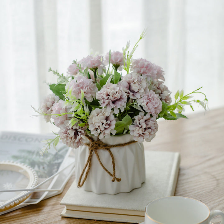 Seidenblumenarrangement in einem mit Schnur umwickelten Keramikpflanzer als Tischmittelpunkt