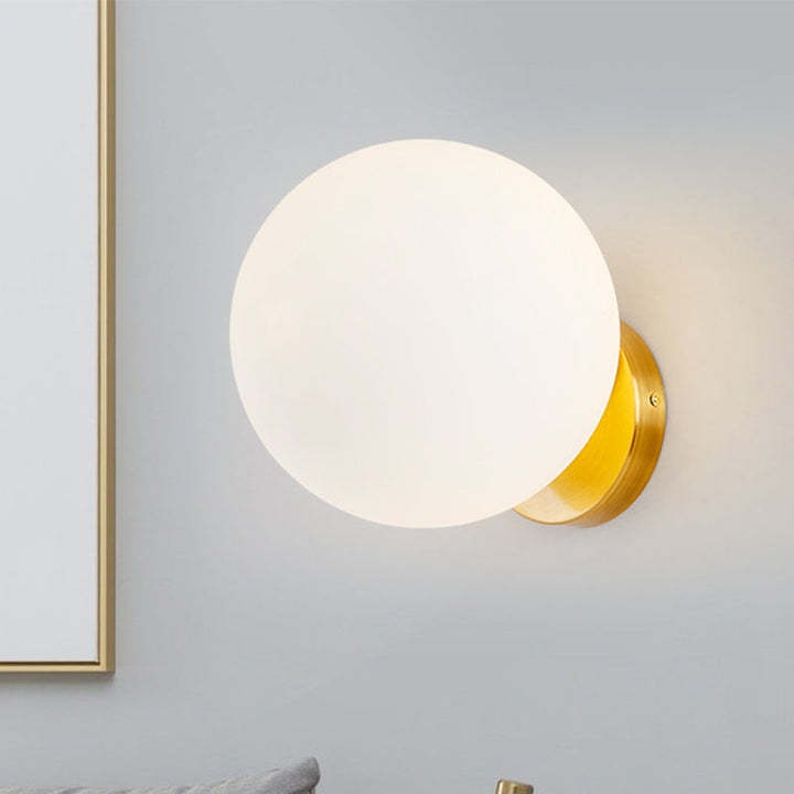 Runde Glaswandleuchte mit goldener Halterung neben Spiegel und Bett