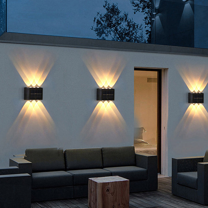 Drei Solar-Außenwandleuchten mit Up-&-Down-Licht an weißer Wand über Outdoor-Lounge

