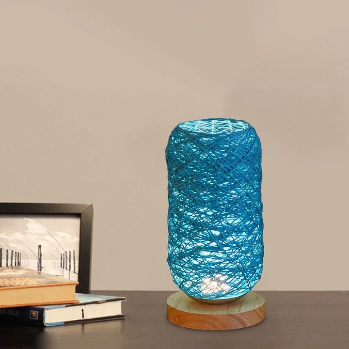 Blaue Tischlampe mit geflochtenem Lampenschirm und Holzfuß auf Schreibtisch mit Büchern