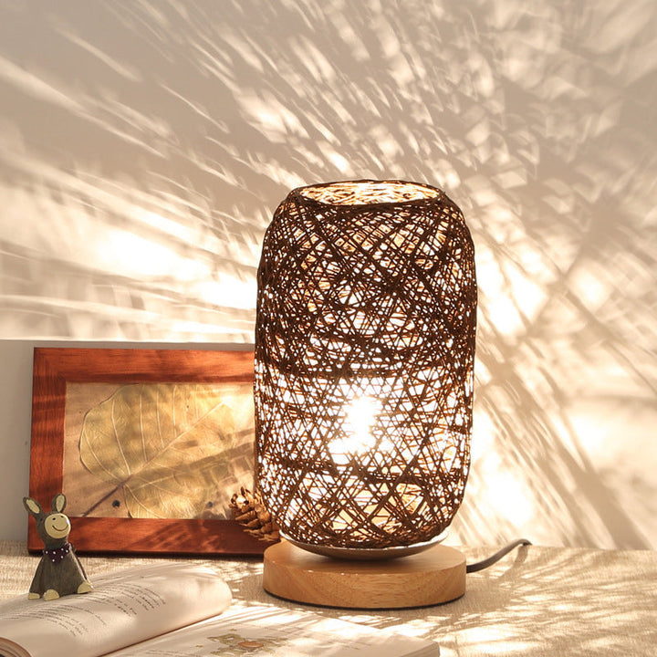 Leuchtende Flechtlampe mit Schattenwurf an der Wand neben Buch und Figur