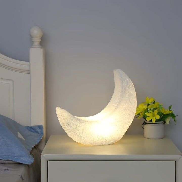 Mondförmige Nachtlampe in Weiß auf Nachttisch mit Blumen neben Bett

