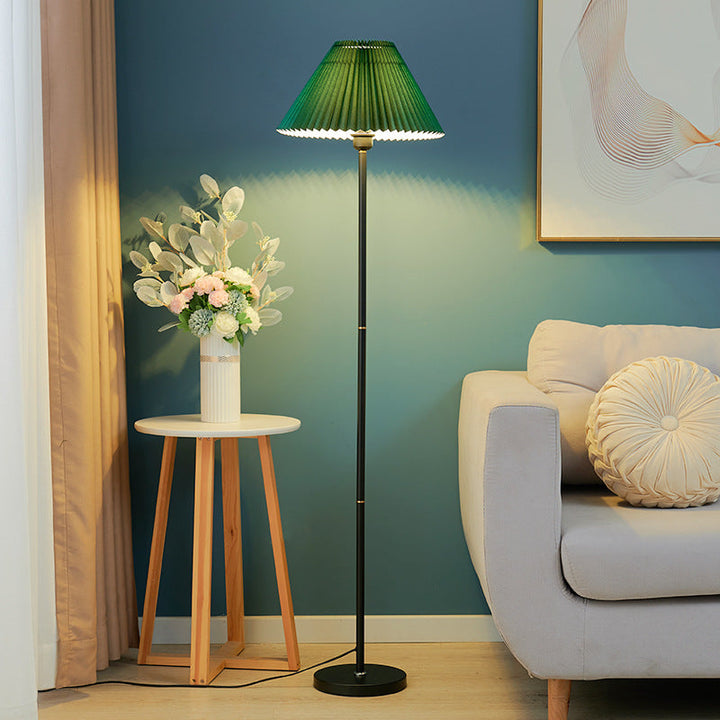 Stehlampe mit grünem Faltenschirm neben Sofa und Holztisch

