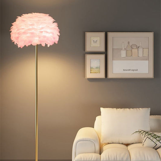 Stehlampe mit rosa Federlampenschirm und goldfarbenem Gestell neben weißem Sofa