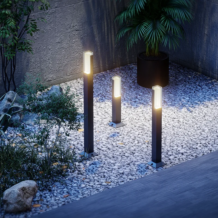 Drei moderne Wegeleuchten mit warmweißem Licht auf weißem Kiesweg im Garten