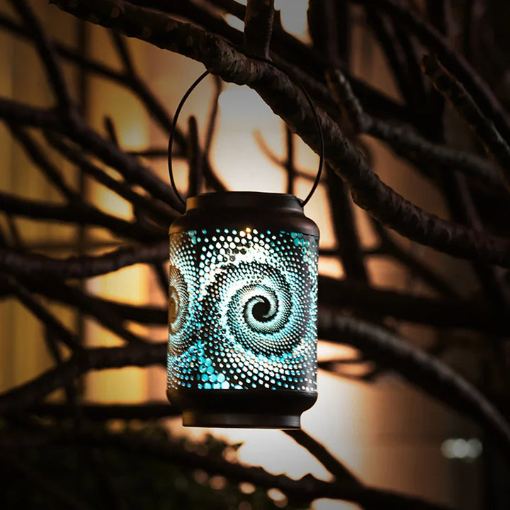 Solarlicht mit blauem Spiralmuster hängt dekorativ zwischen Ästen im Außenbereich
