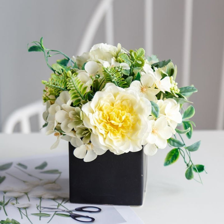 Lebensechte Blumenarrangement in dekorativem quadratischen Pflanzgefäß