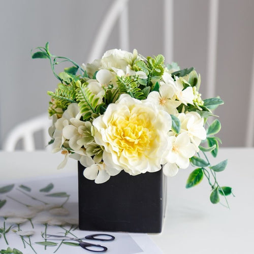 Lebensechte Blumenarrangement in dekorativem quadratischen Pflanzgefäß