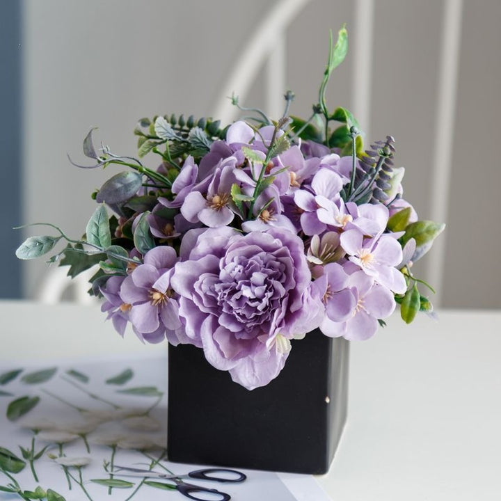 Lebensechte Blumenarrangement in dekorativem quadratischen Pflanzgefäß