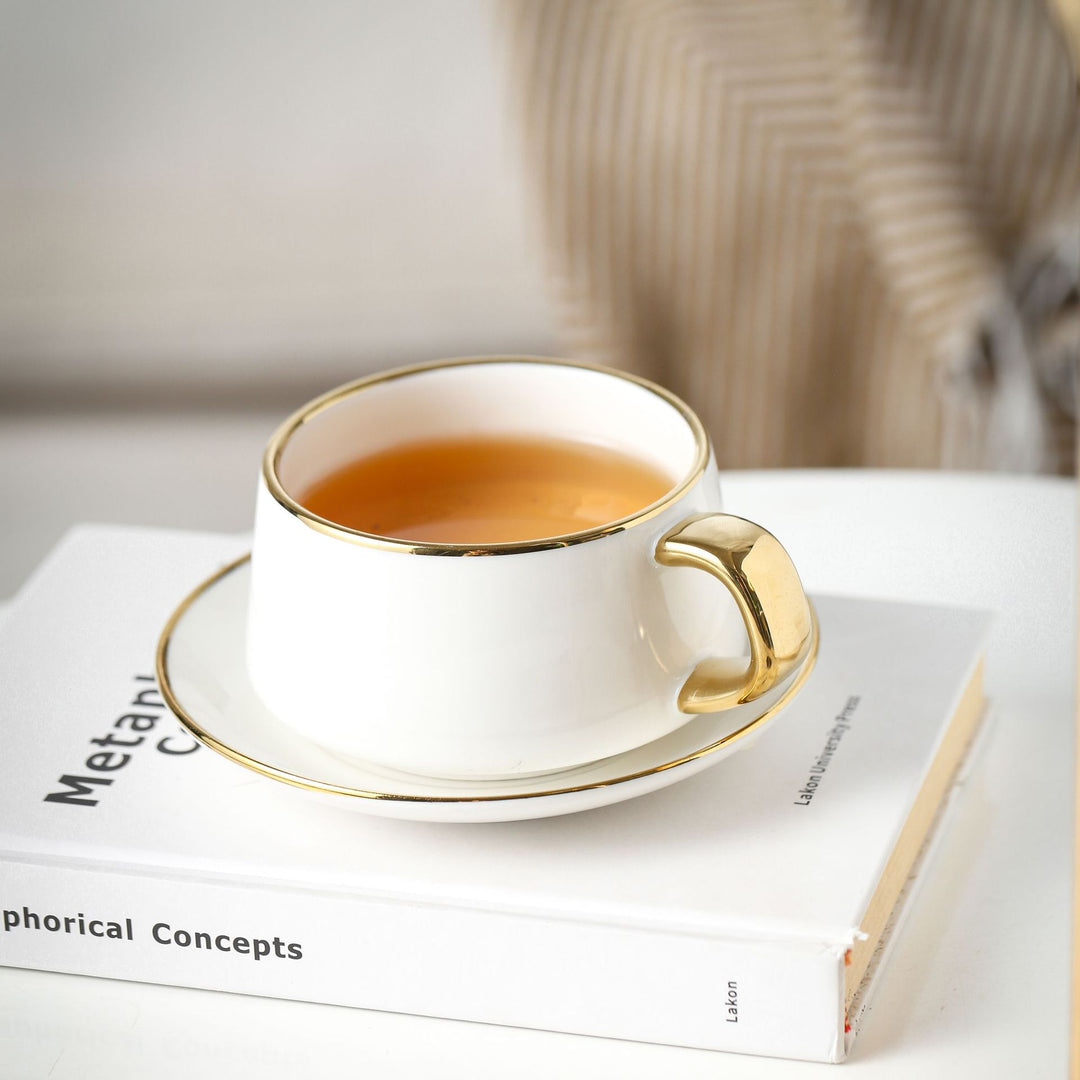 Elegante Porzellan-Tasse mit Untertasse und skulpturellem Goldhenkel